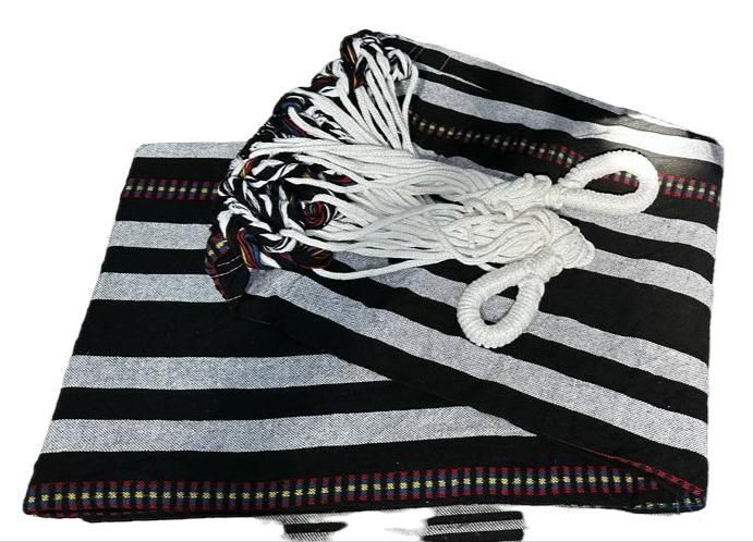 Una hamaca plegada con rayas negras y grises, cuerdas blancas para colgar y bordes decorativos tejidos en los extremos.