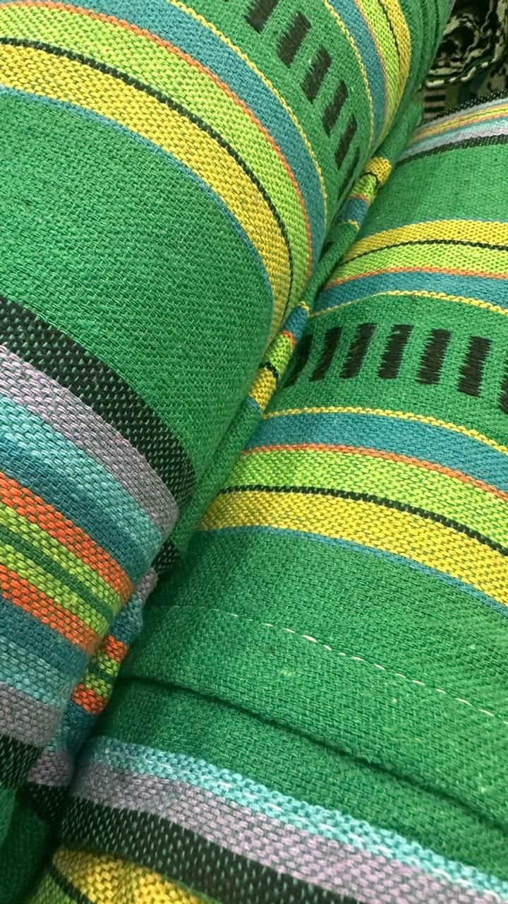Primer plano de una tela verde enrollada firmemente con rayas horizontales en amarillo, naranja, azul y negro.