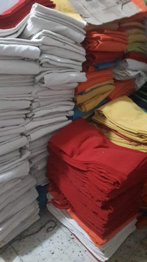 Varias pilas de telas o toallas blancas, rojas, amarillas y naranjas dobladas y organizadas en el suelo.