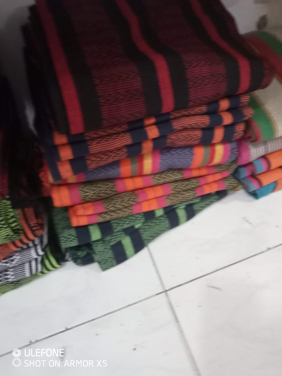 Telas apiladas y dobladas con diversos estampados de rayas de colores, descansan sobre un suelo de baldosas.