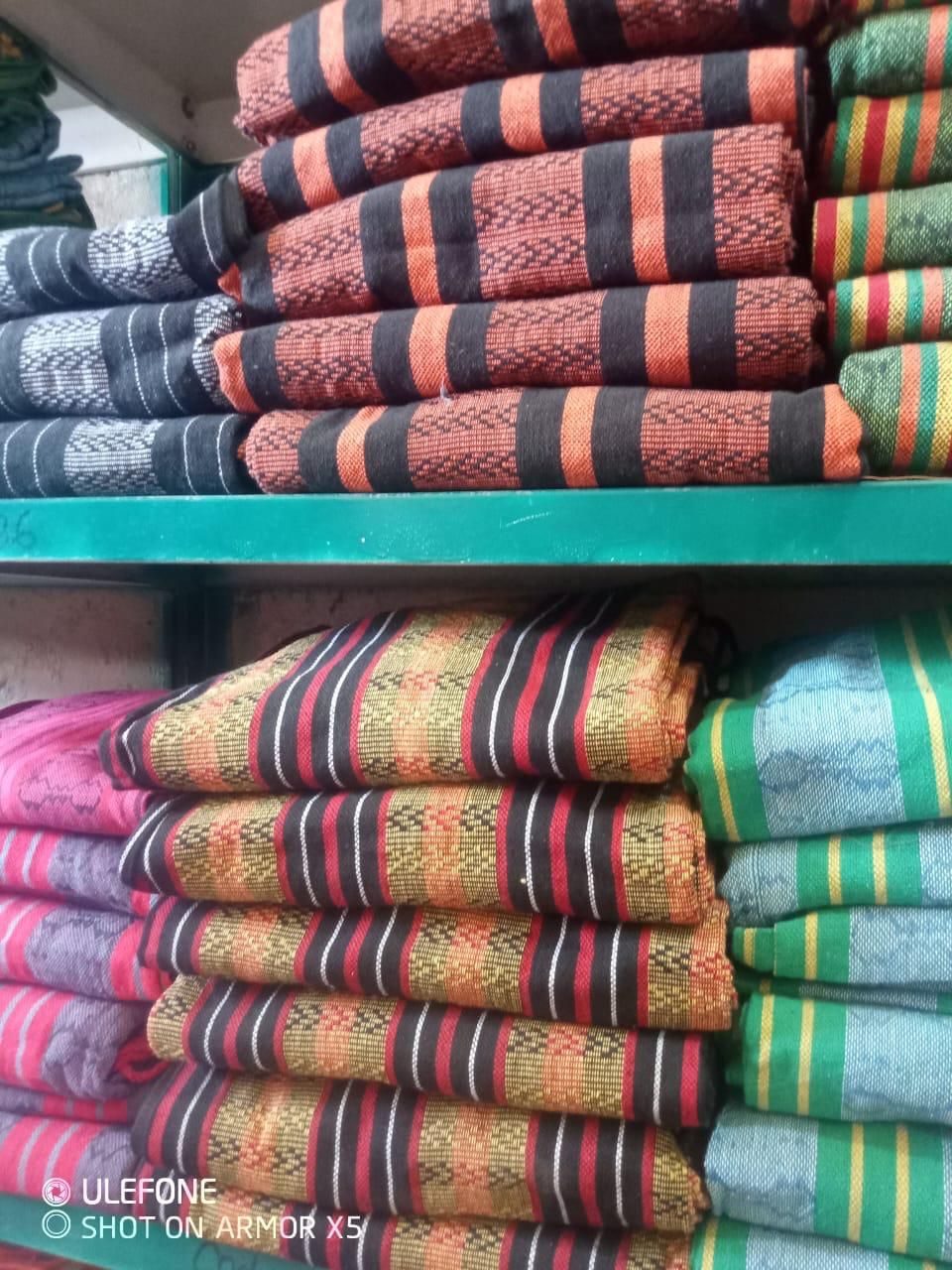 Montones de telas dobladas y estampadas con rayas naranjas, negras, rojas y verdes en estantes de madera de una tienda.