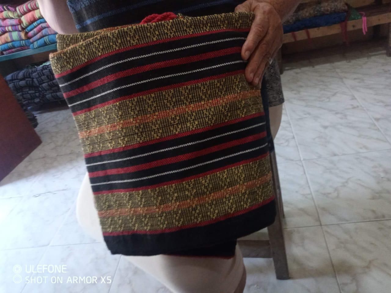 Una persona sostiene un tejido hecho a mano con franjas alternas de colores negro, rojo y marrón dorado.