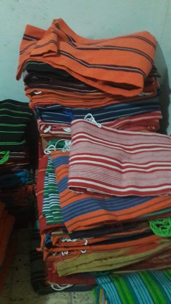 Una pila alta y desorganizada de telas a rayas de colores, dobladas y en tonos naranja, azul, verde y rojo.