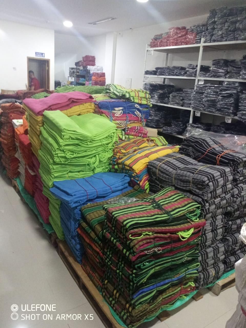 Alfombras y textiles de colores apilados en estantes y paletas en un almacén bien iluminado.