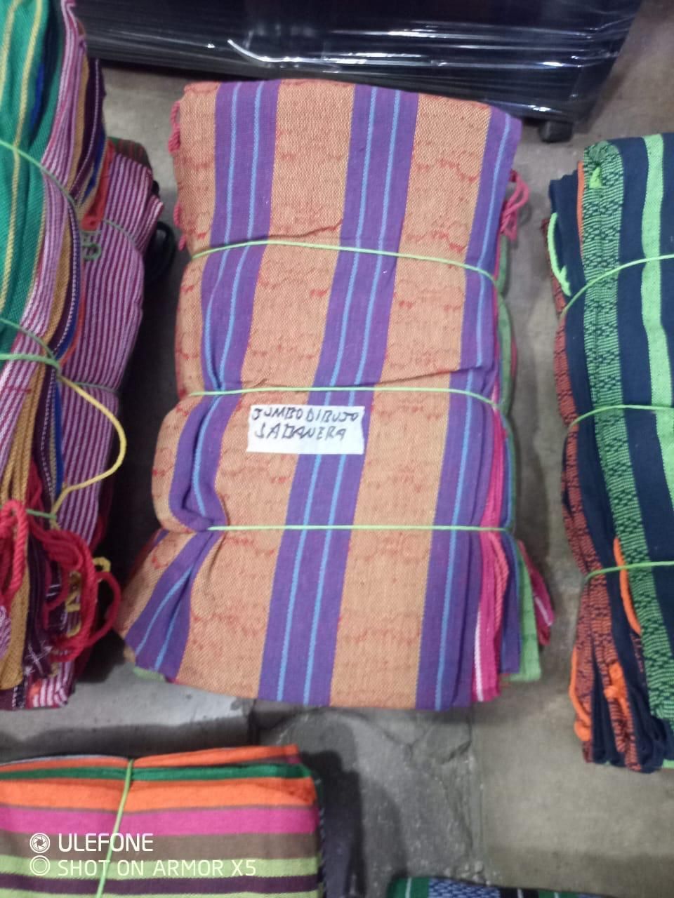 Paquetes de telas a rayas de colores, dobladas y en tonos naranja, morado y verde, apilados en el suelo.