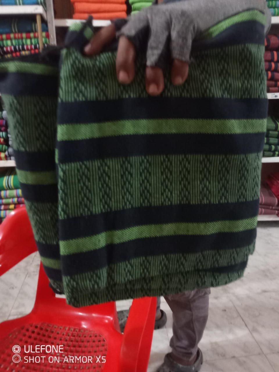 Una persona sostiene una tela doblada con estampado verde y negro en una tienda con estantes de textiles al fondo.