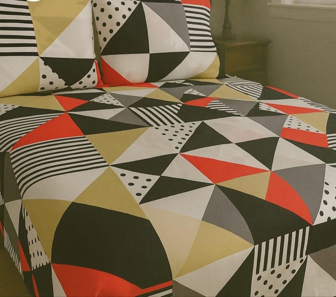 Una cama con una colcha de estampado geométrico con triángulos en negro, blanco, rojo y amarillo mostaza.