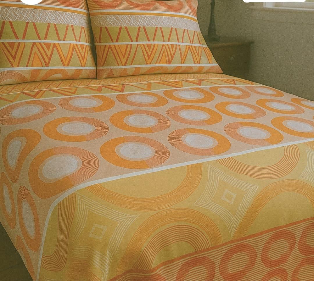 Una cama con una colcha de estampado geométrico y almohadas a juego en tonos cálidos de naranja, dorado y blanco.