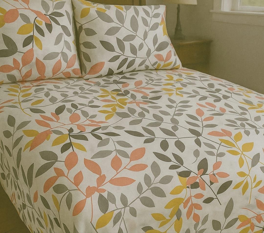 Una cama con un edredón blanco y almohadas con un estampado de hojas en tonos amarillos, coral y grises.