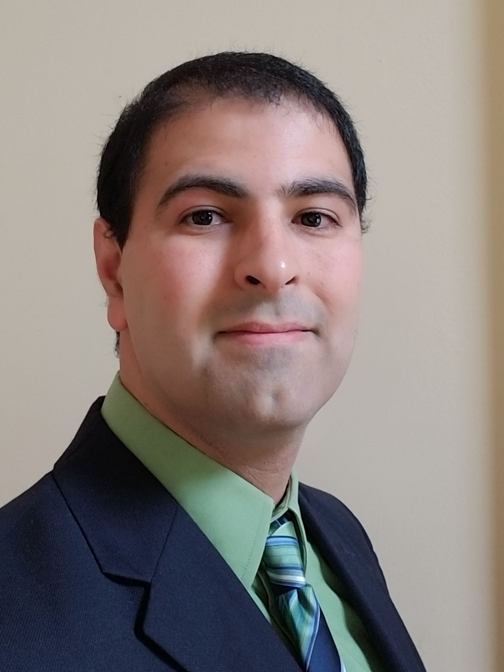 Portrait of a smiling person in a dark suit, green shirt, and striped tie against a plain wall