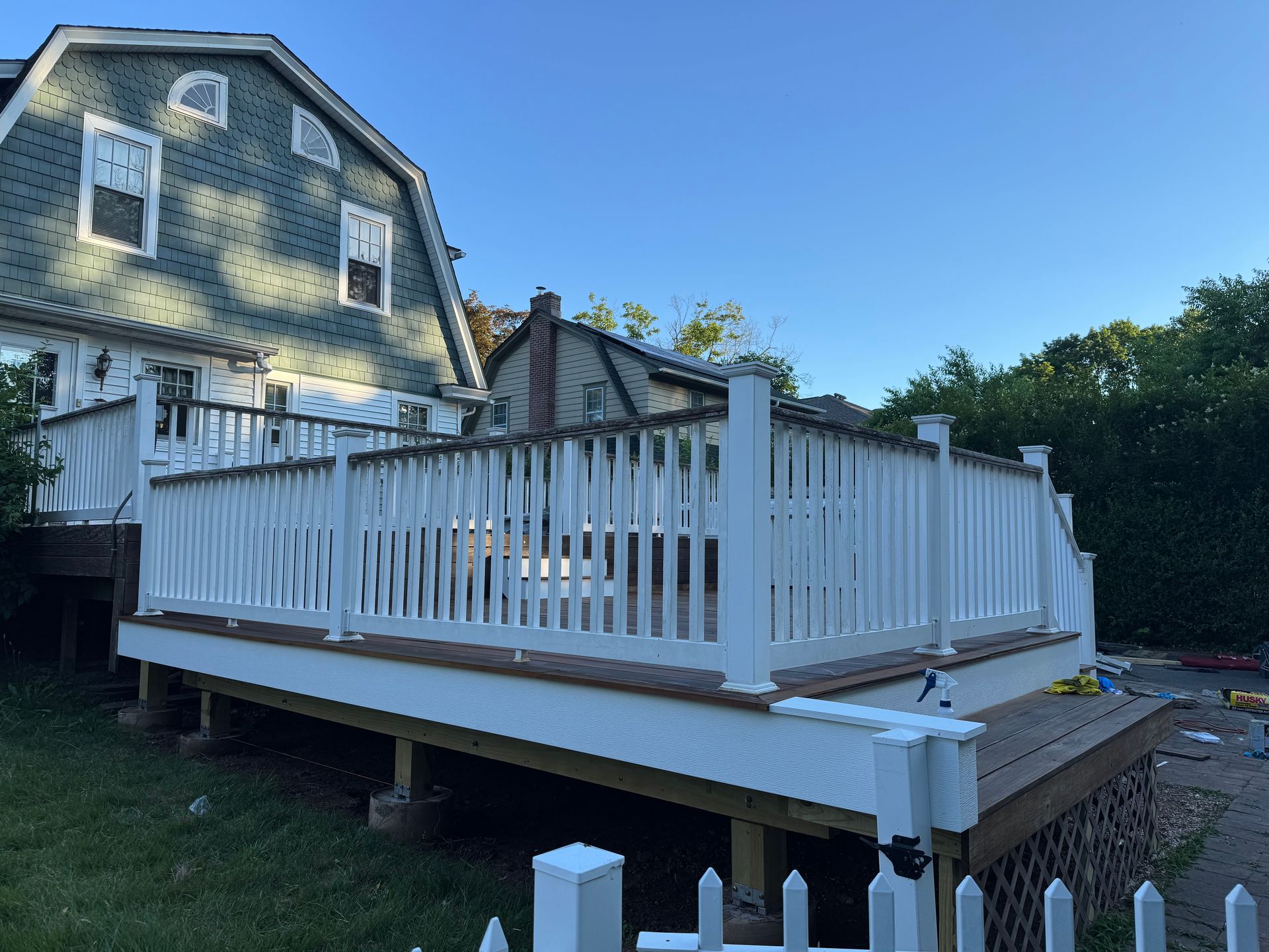 A large white deck with a white picket fence in front of a house.