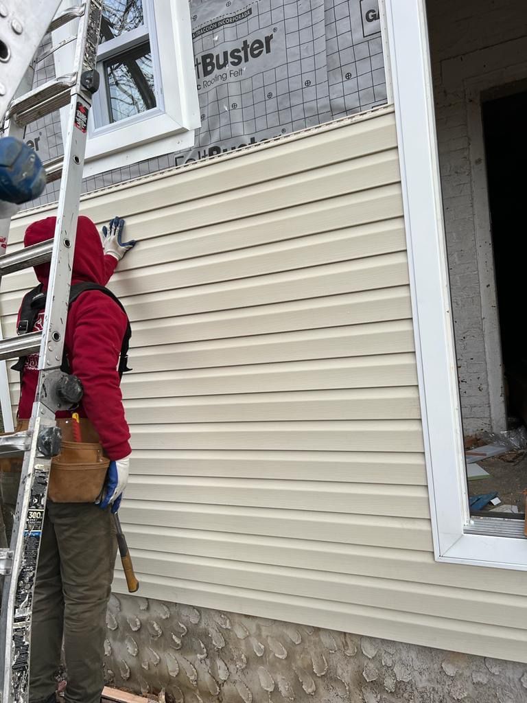 A man is installing siding on the side of a house.