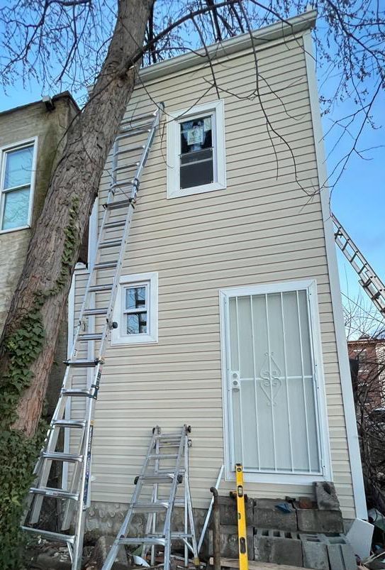 A ladder is sitting on the side of a house next to a tree.