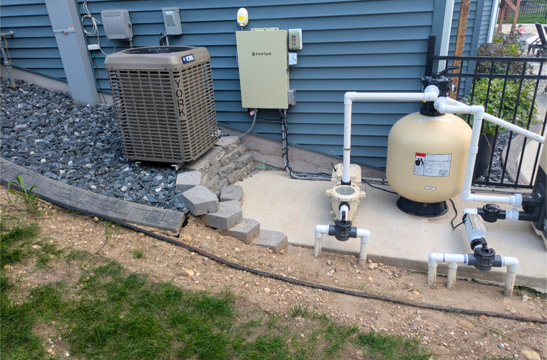 A pool pump and sand filter system on a concrete pad next to an HVAC unit, installed against a blue-sided house.