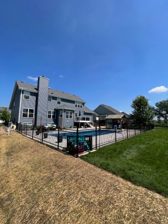 A two-story grey house with a swimming pool and fence in the backyard under a bright blue sky.