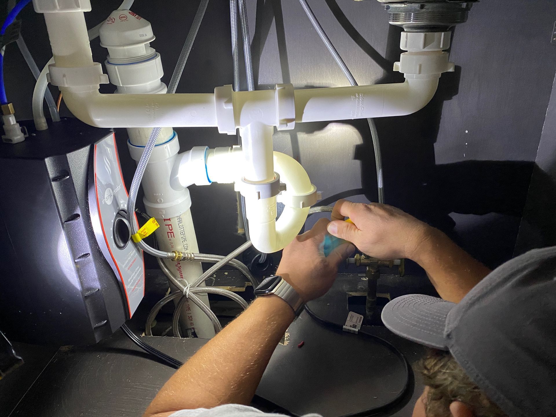Plumber repairs a leaking sink drain pipe under a white bathroom sink with a wrench