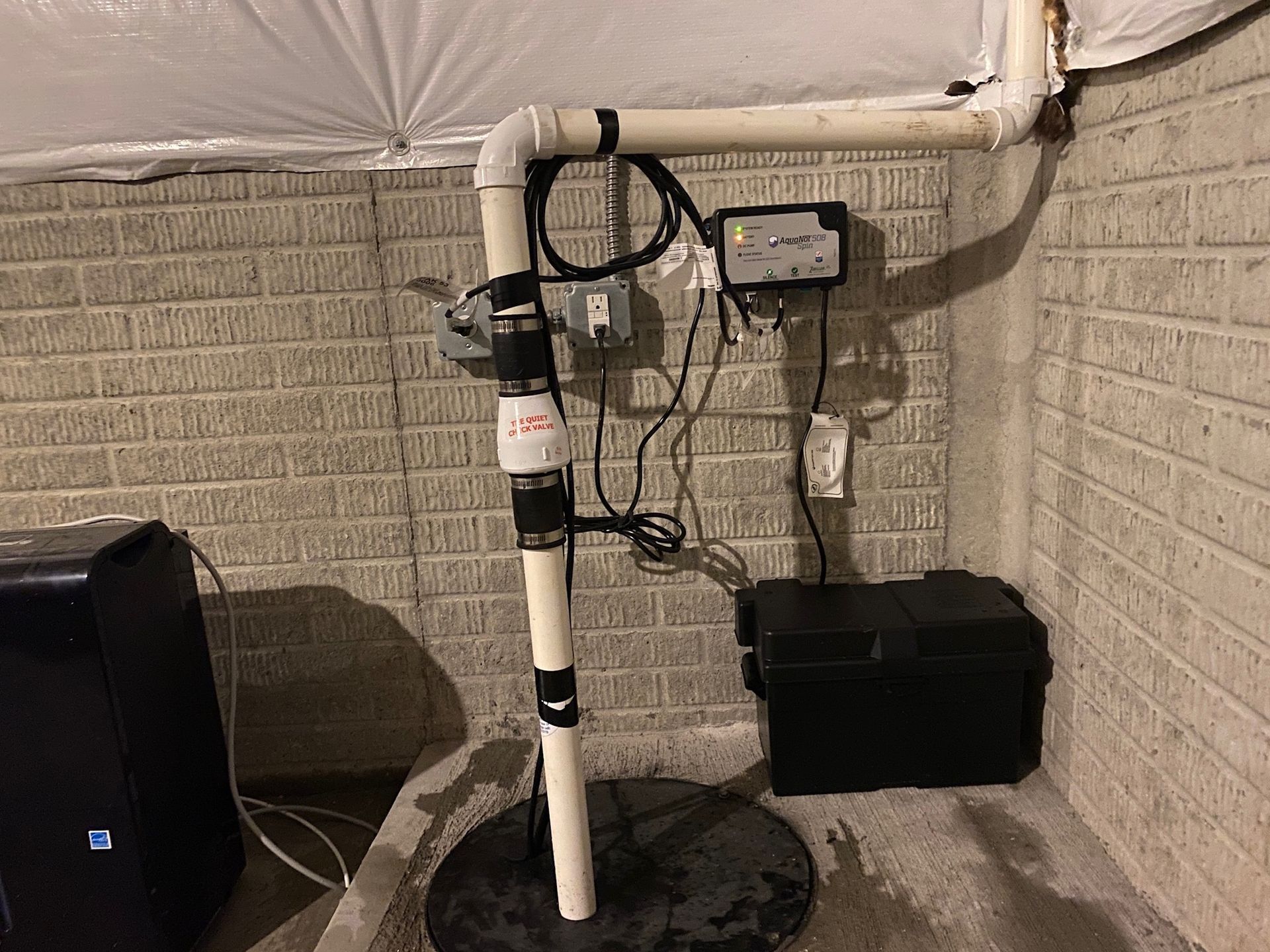 Basement floor with open sump pit and PVC pipes, water pooled around the opening.