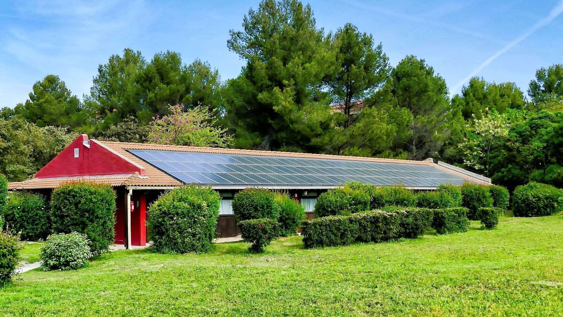 A house with solar panels on the roof is surrounded by trees and bushes.