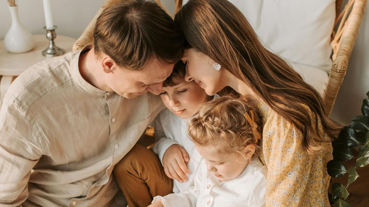 A family is sitting on the floor looking at a book together.
