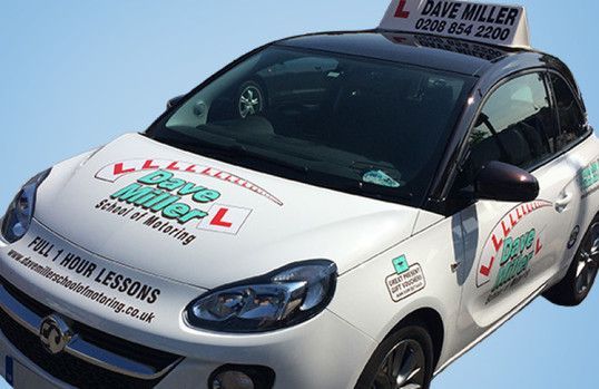 a white car with a sign on top that says dave miller school of motoring .
