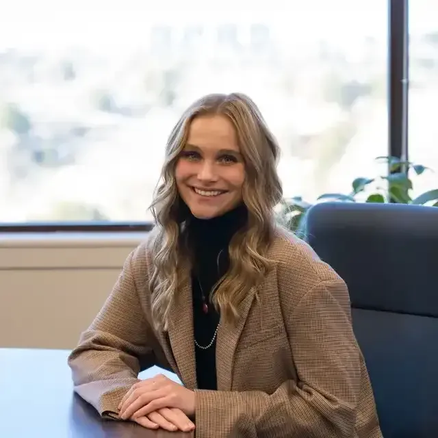 A woman is smiling while sitting at a desk in front of a window.