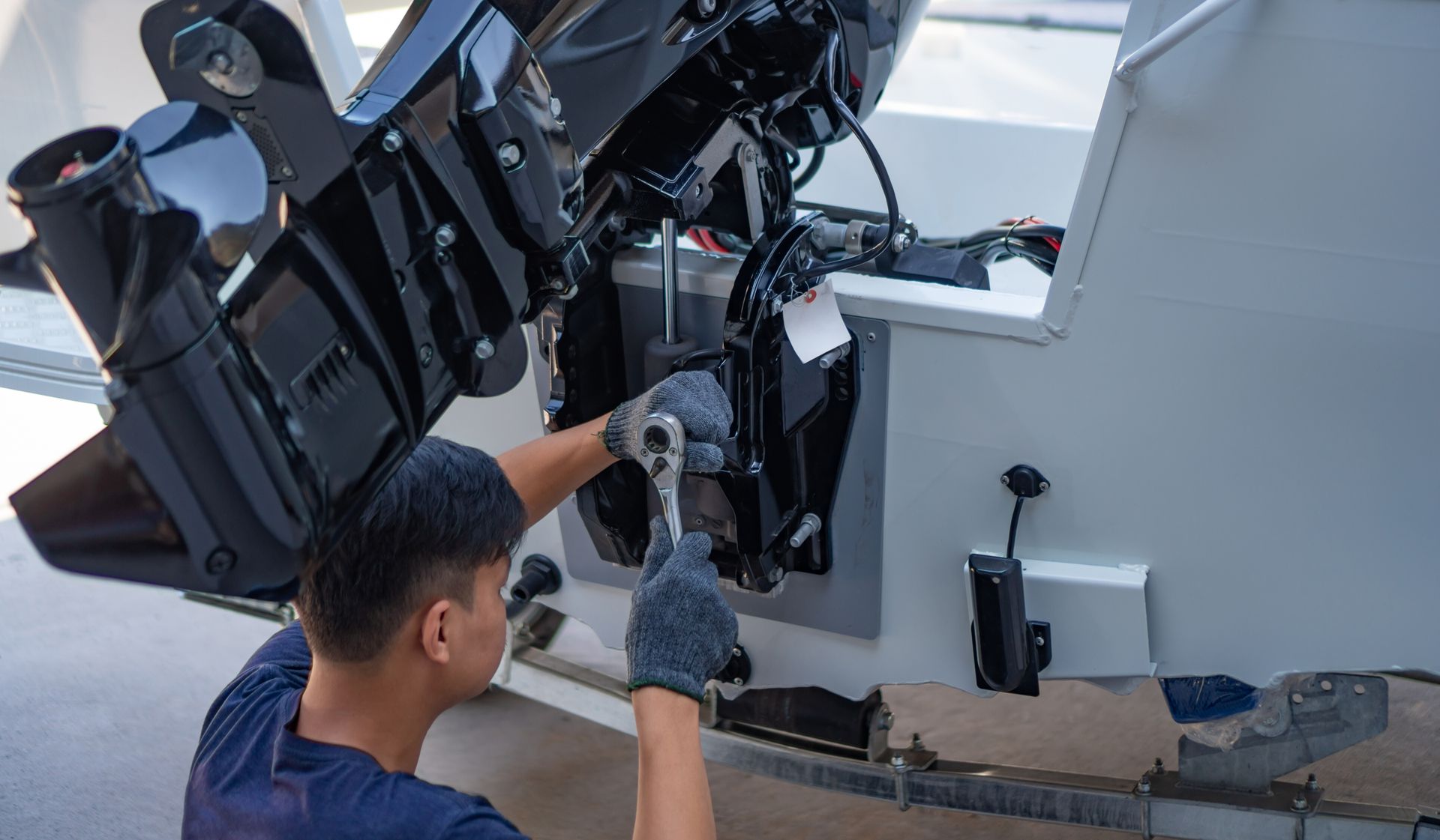 Person inspecting a boat engine near the stern, with a black outboard motor and white hull. Person inspecting a boat engine near the stern, with a black outboard motor and white hull.
