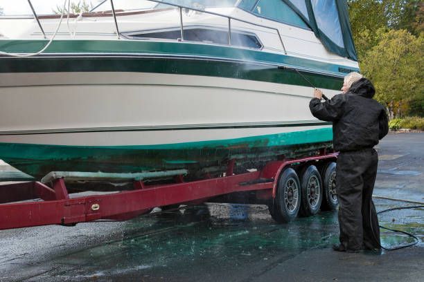 Person pressure washing boat hull on trailer during boat maintenance and cleaning outdoors marina.
