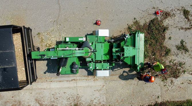 Top-down view of a green agricultural machine beside a gravel road, with pumpkins and tools nearby