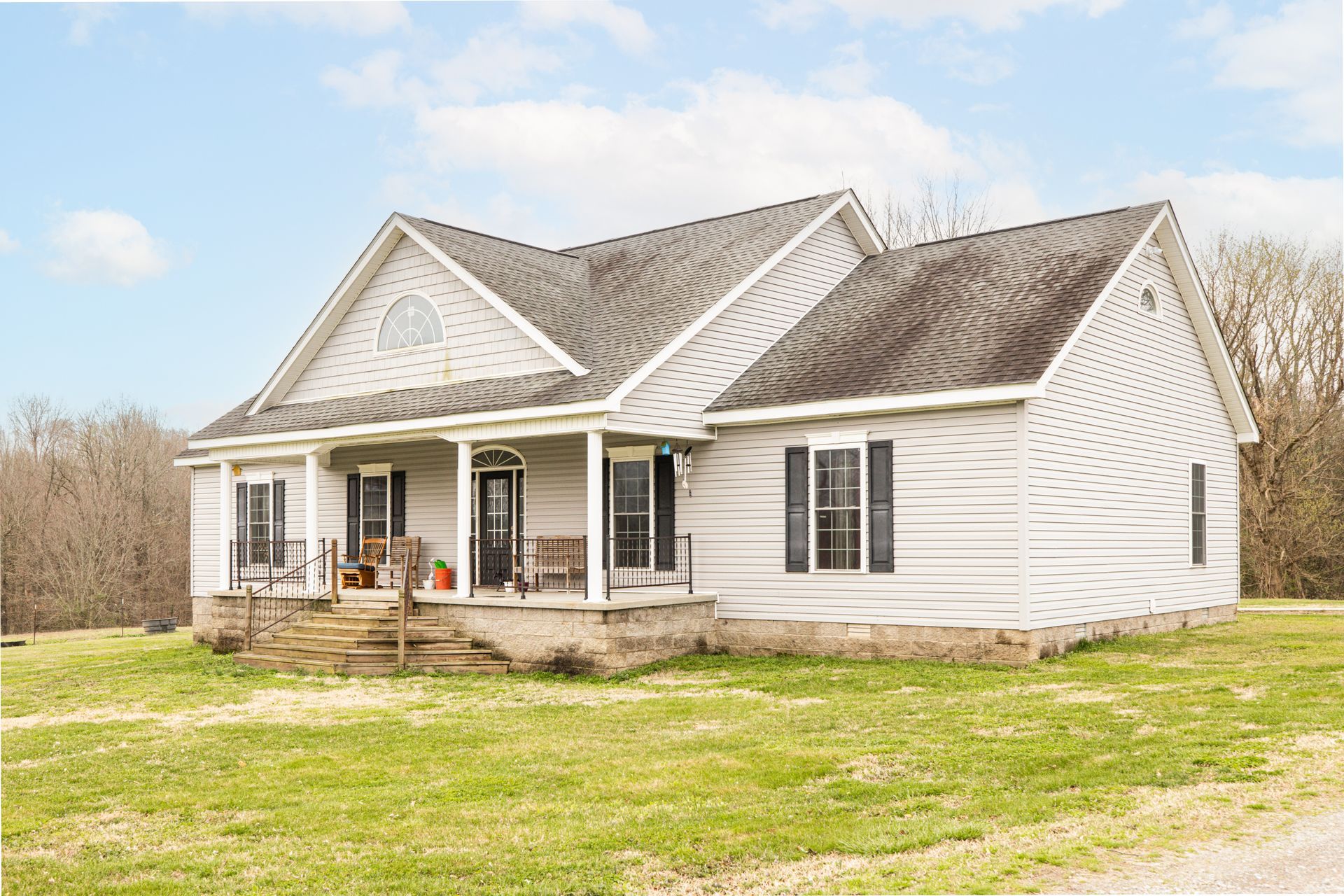 White house with a front porch and gabled roof in a grassy yard under a bright sky