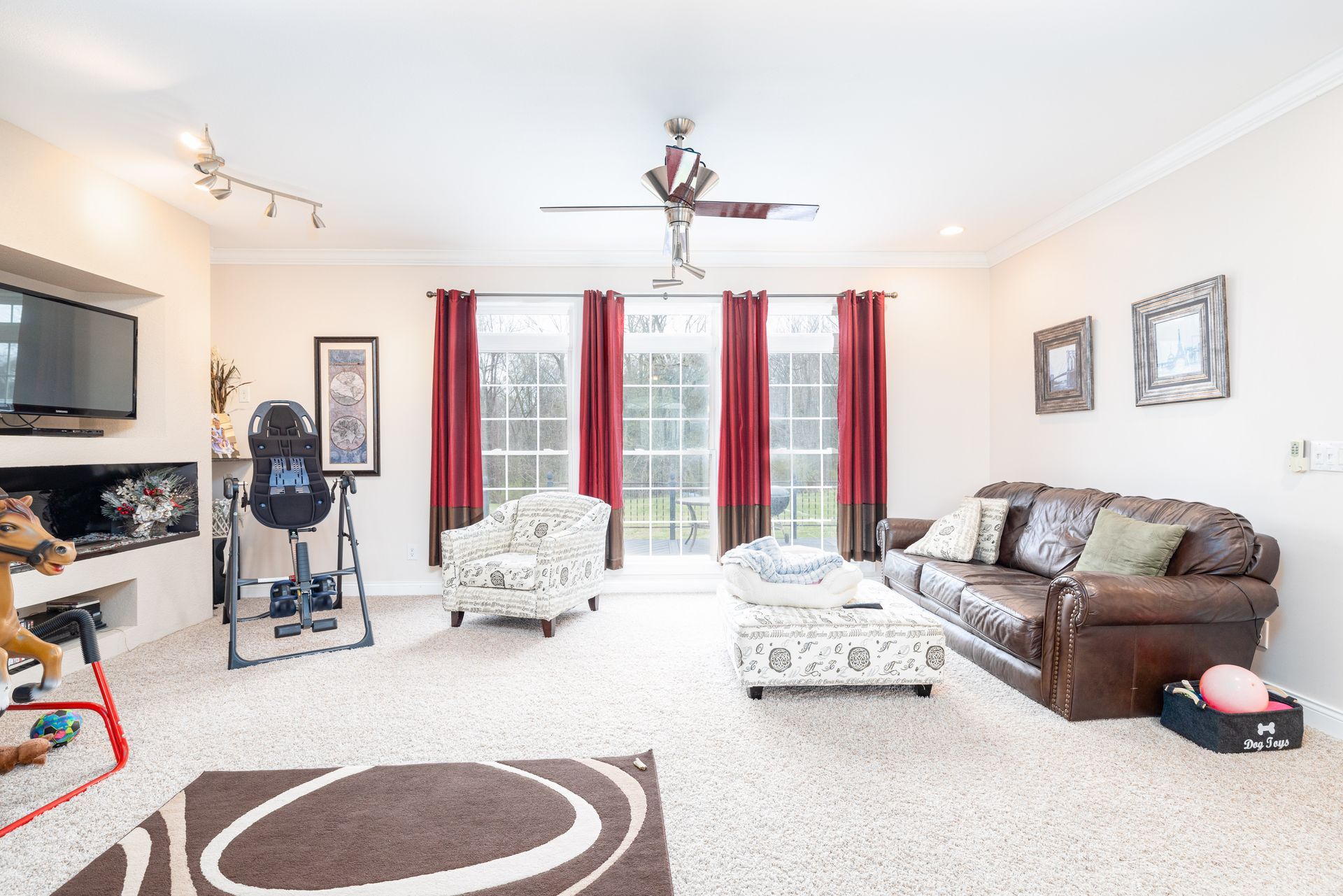 Bright living room with brown sofa, white ottoman, TV, and red curtains by glass doors