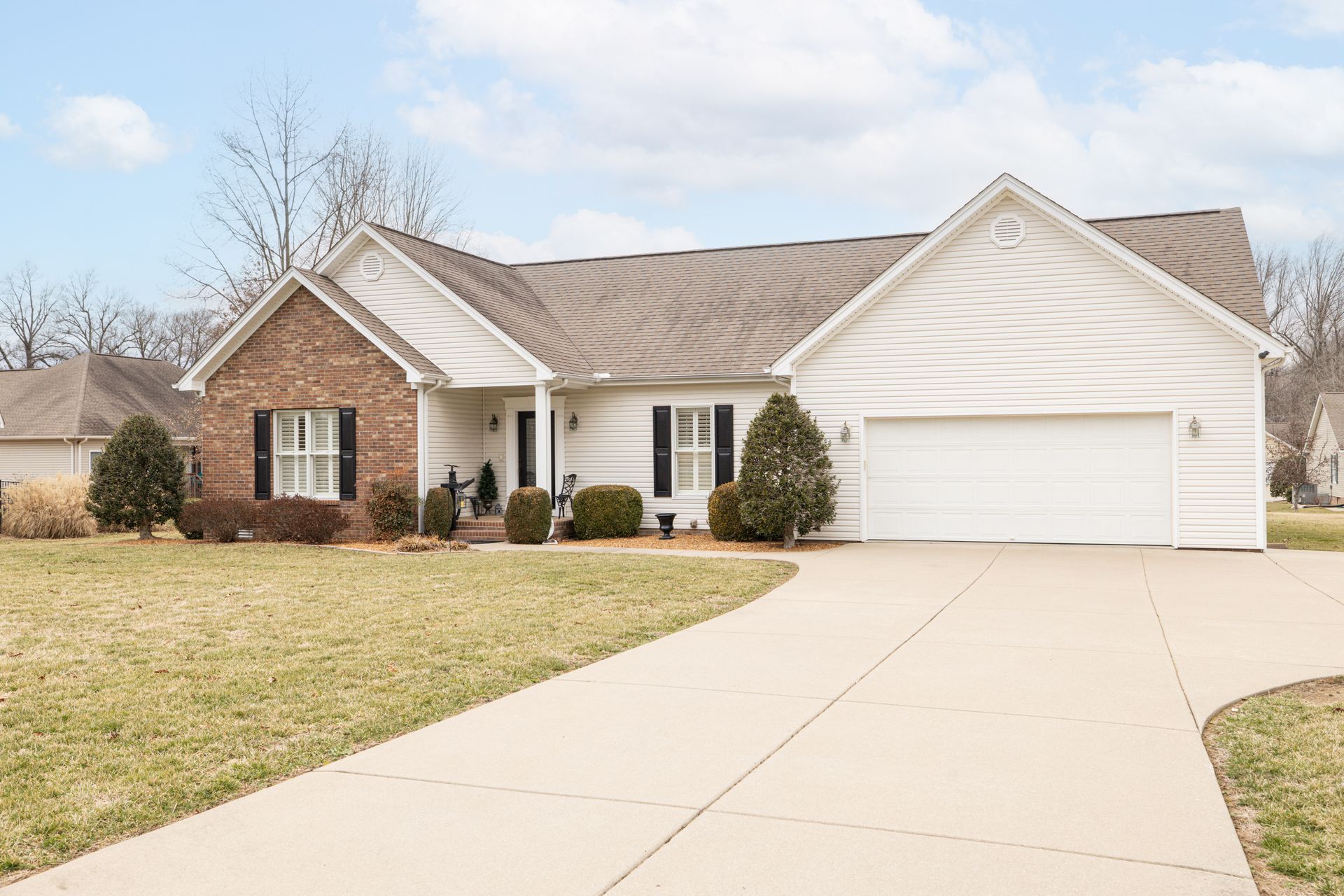Suburban house with brick and beige siding, two-car garage, and a curved driveway under a clear sky