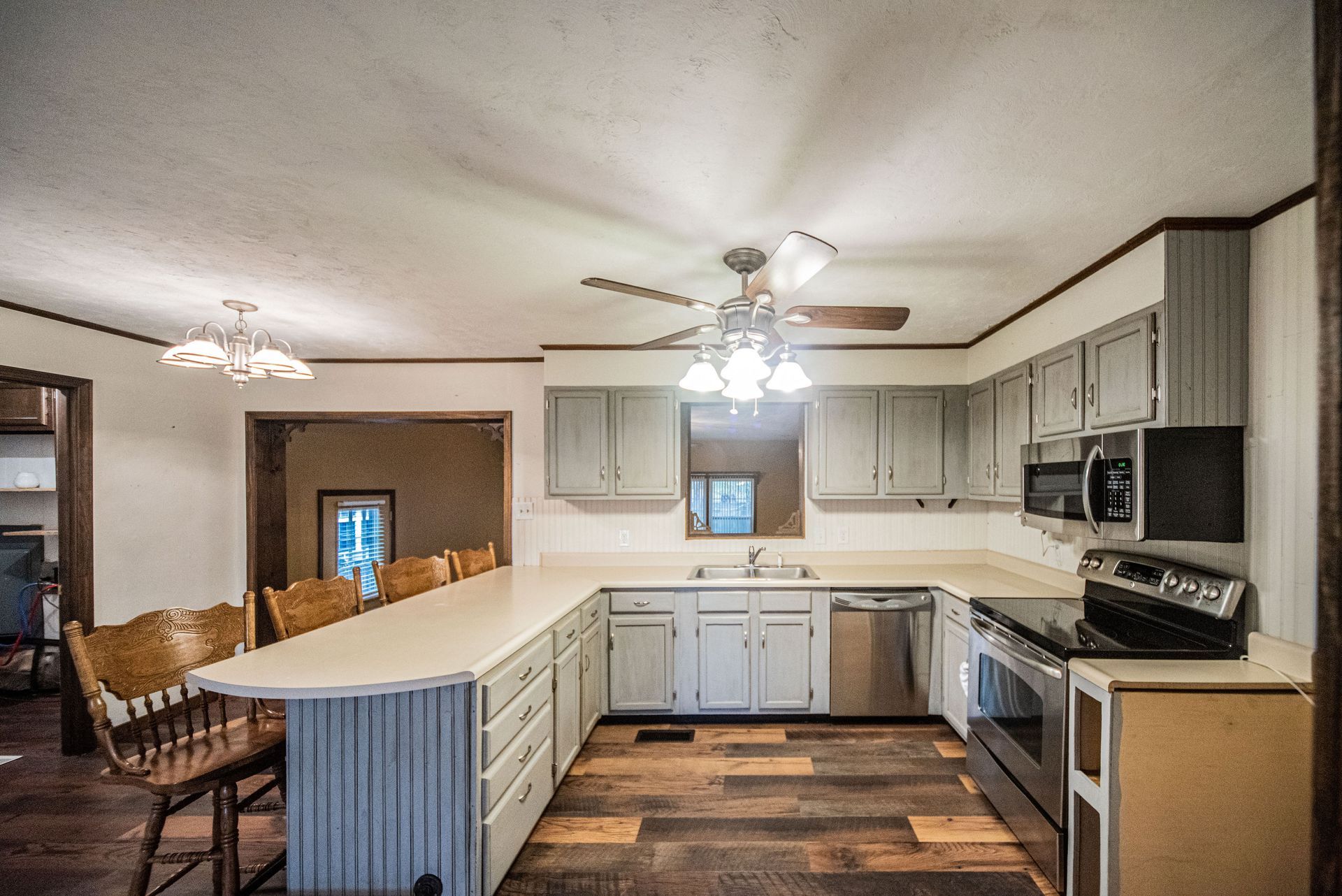 Bright kitchen with white cabinets, stainless appliances, island counter, and ceiling fans; dining area visible beyond.