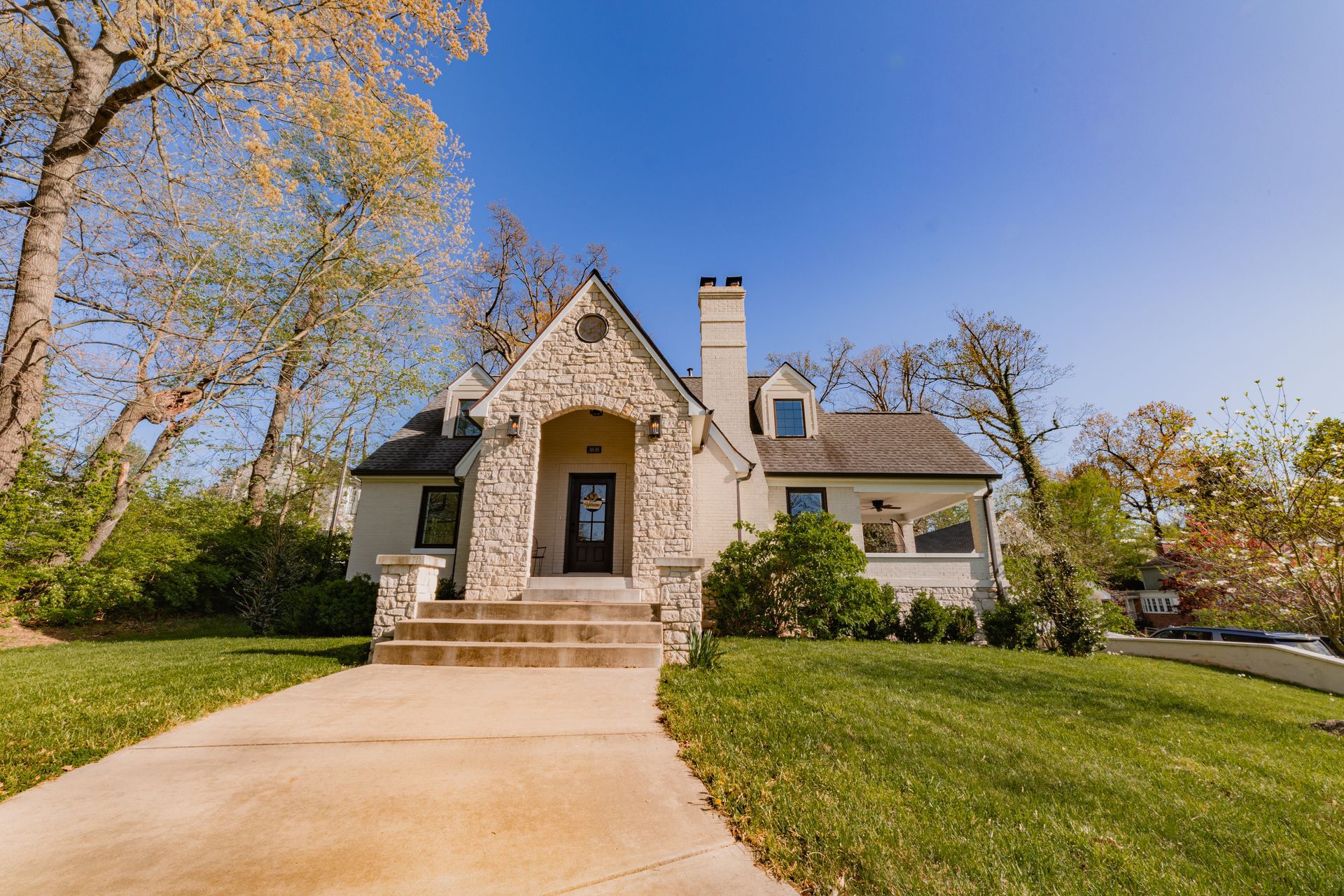 Stone house with front steps, green lawn, and trees under a clear blue sky