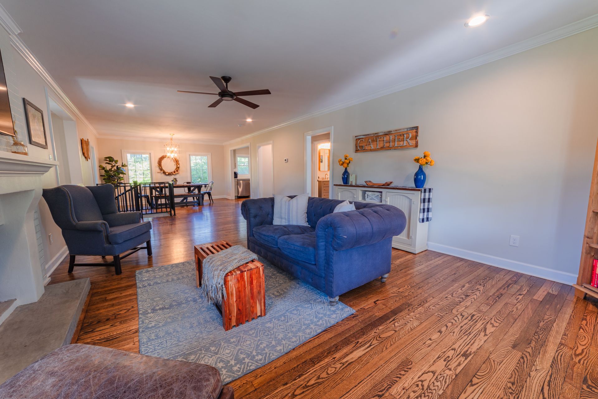 Bright living room with blue sofa, chairs, wood floor, and dining area in the background