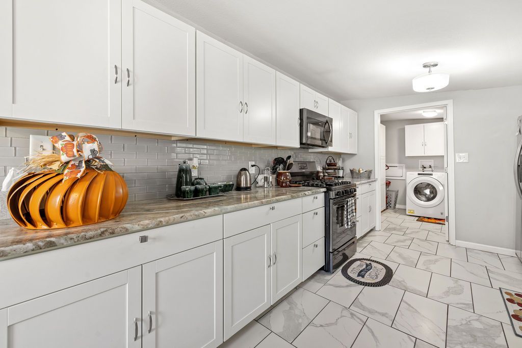 Bright white kitchen with long countertops, pumpkin decor, and a patterned floor leading to a laundry room.