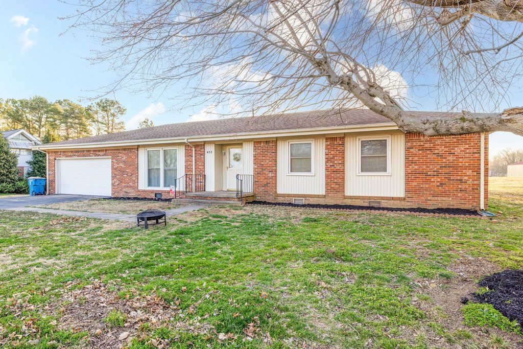 Single-story brick house with a garage, large leafless tree, and grassy front yard.