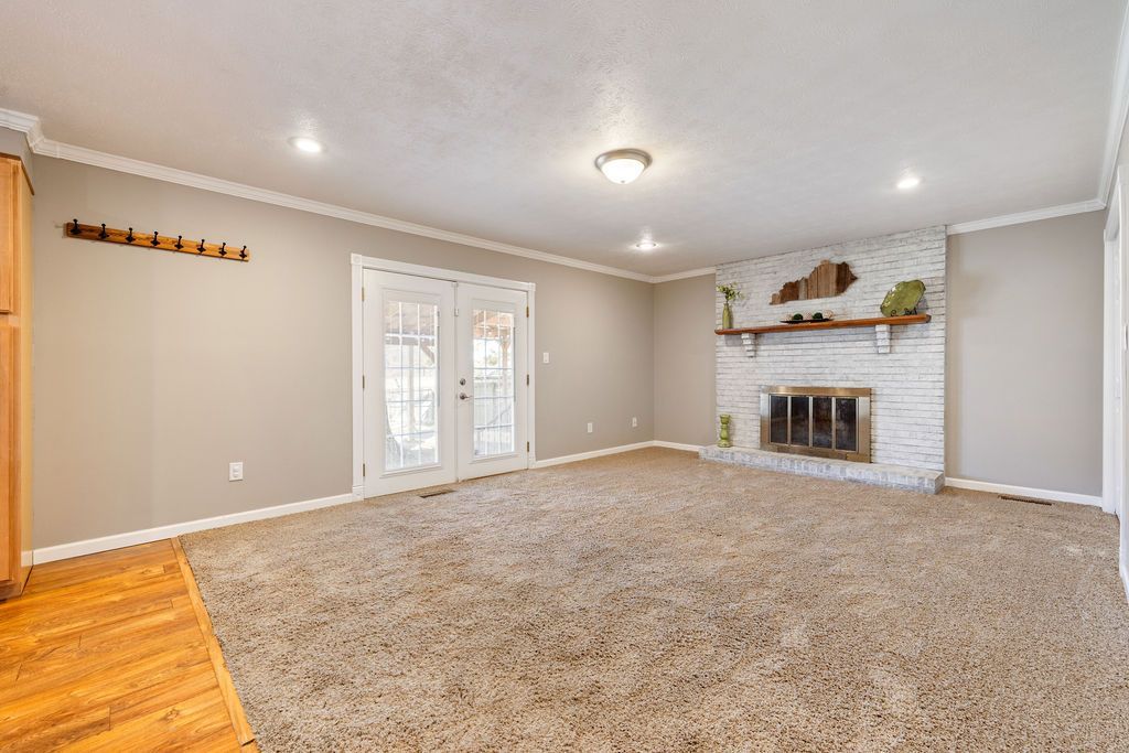 Empty beige living room with carpet, fireplace, and French doors to a patio