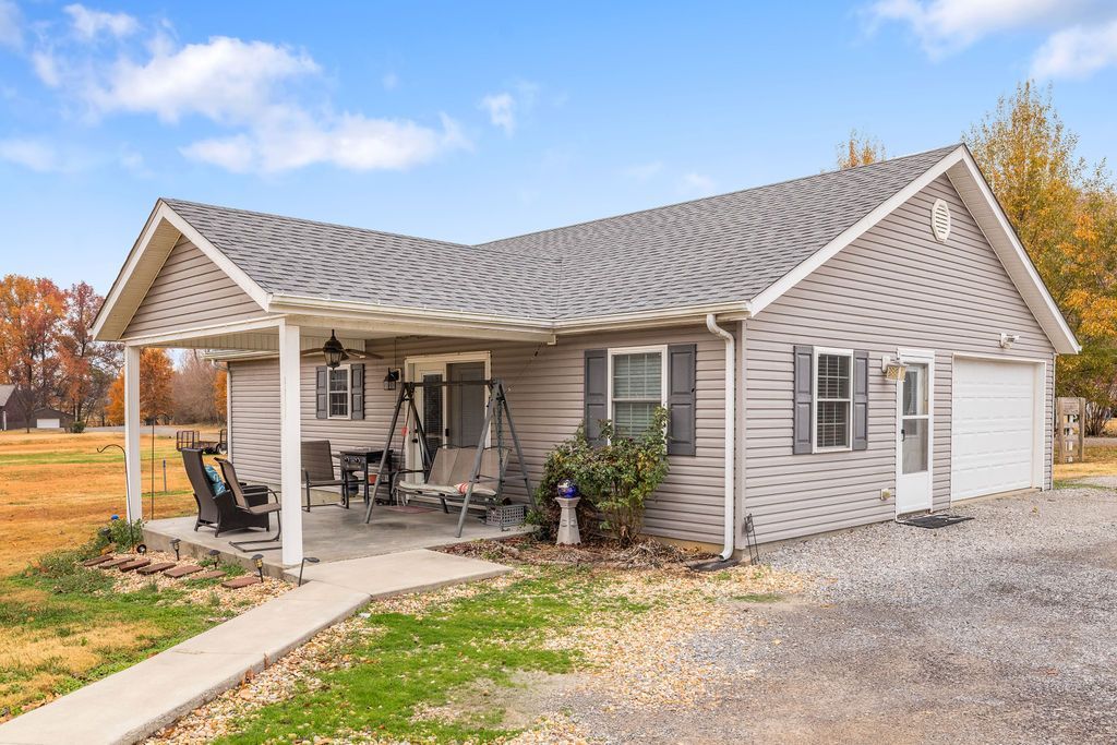 Small white cottage with a covered porch and gravel driveway in a rural setting