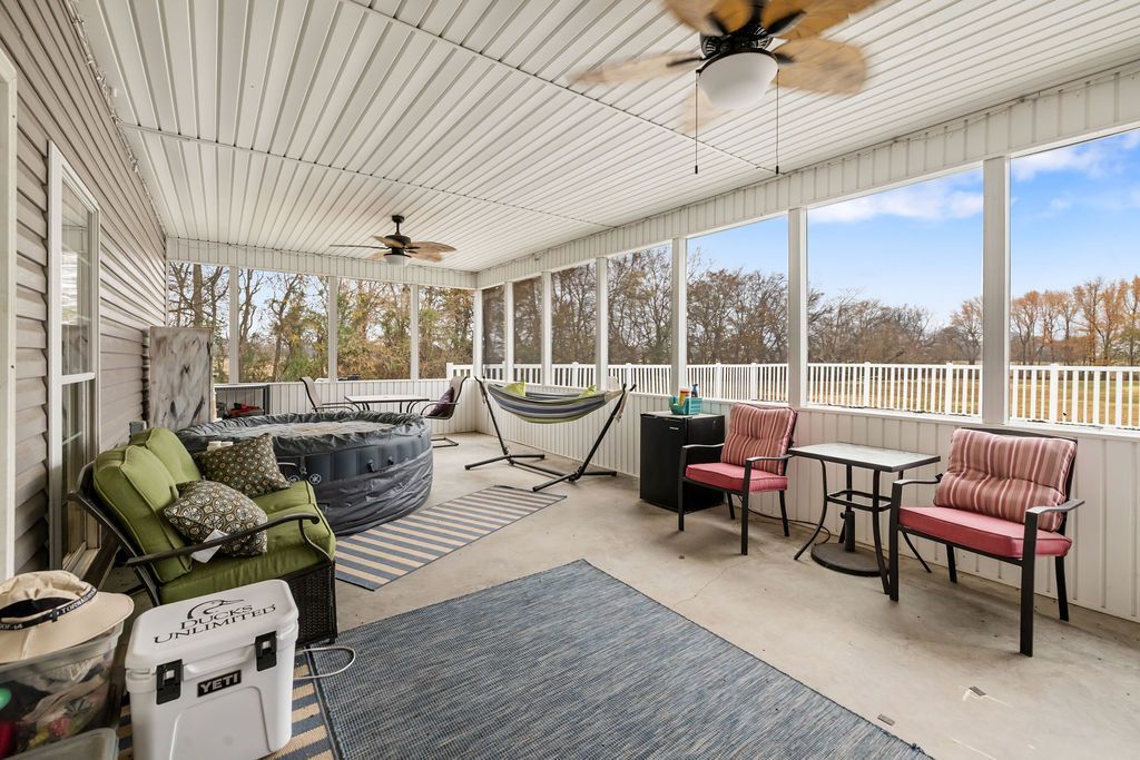Screened porch with wicker sofa, rocking chairs, hammock, rug, and ceiling fans overlooking trees.