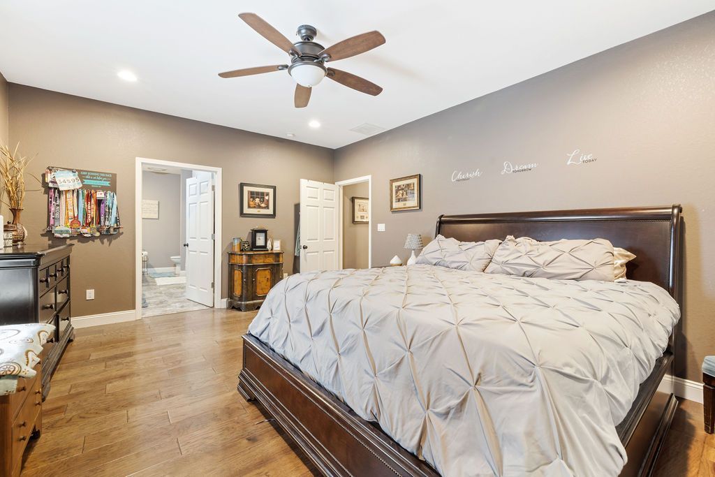 Spacious bedroom with a large bed, ceiling fan, hardwood floor, and open doorway to a hallway