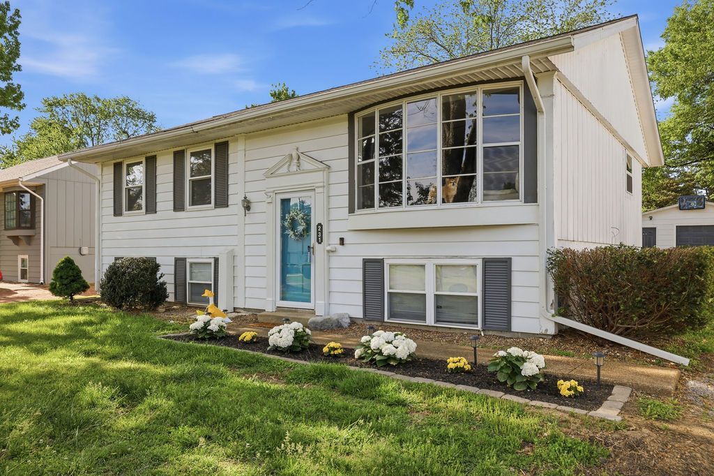 White split-level house with blue front door, bay windows, and a flower bed in front
