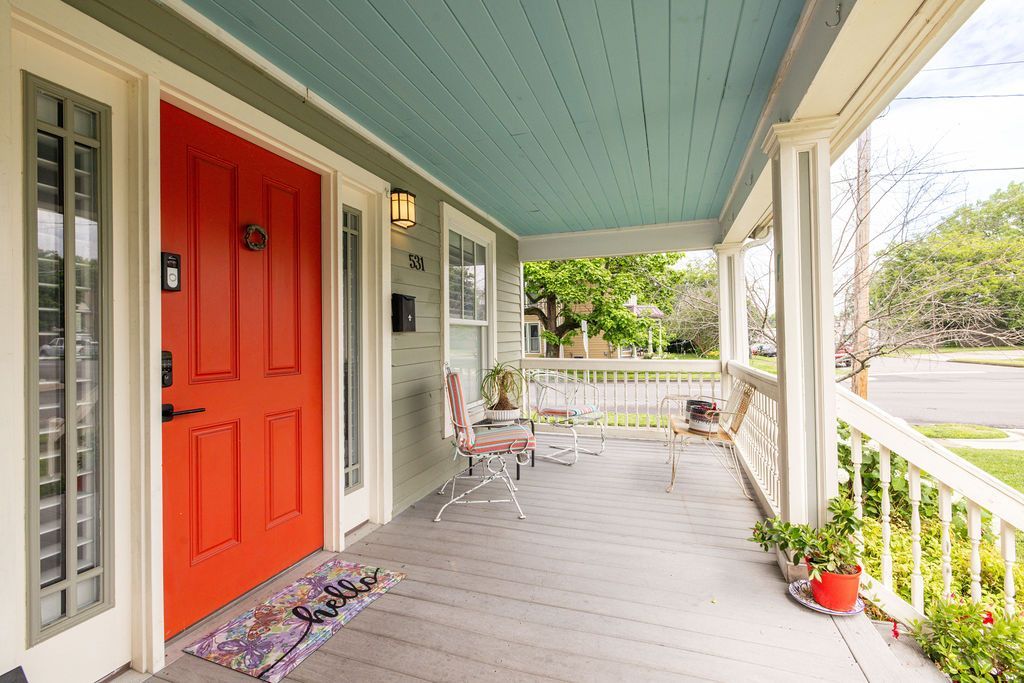 Front porch with bright red door, teal ceiling, white railing, and potted plants.