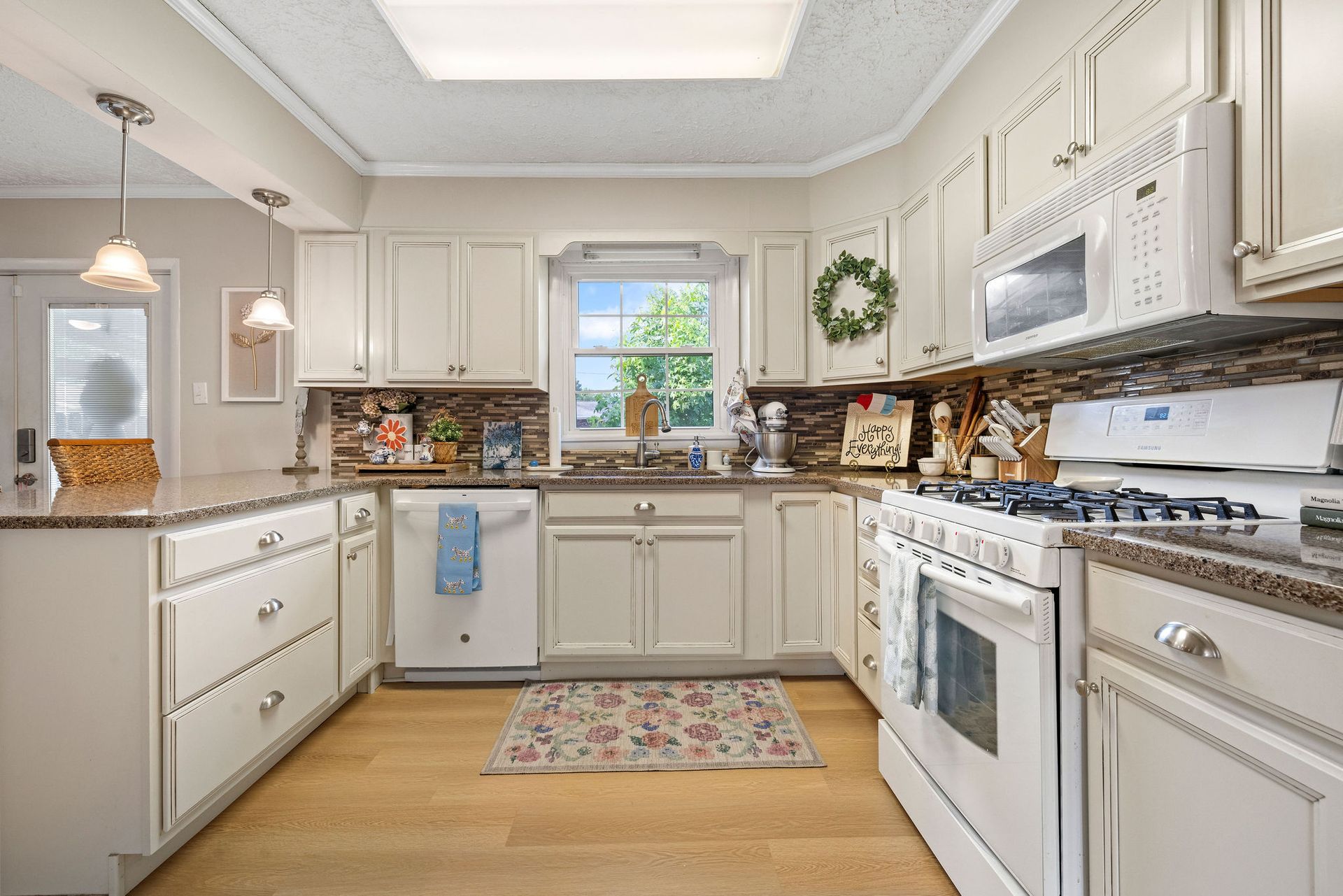 Bright white kitchen with gas stove, farmhouse sink, window, and light wood floor