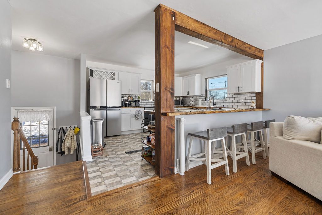 Bright open kitchen and living room with wood floors, bar stools, and a beige sofa