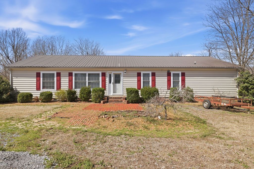 Single-story white house with red shutters, a front lawn, and leafless trees under a blue sky