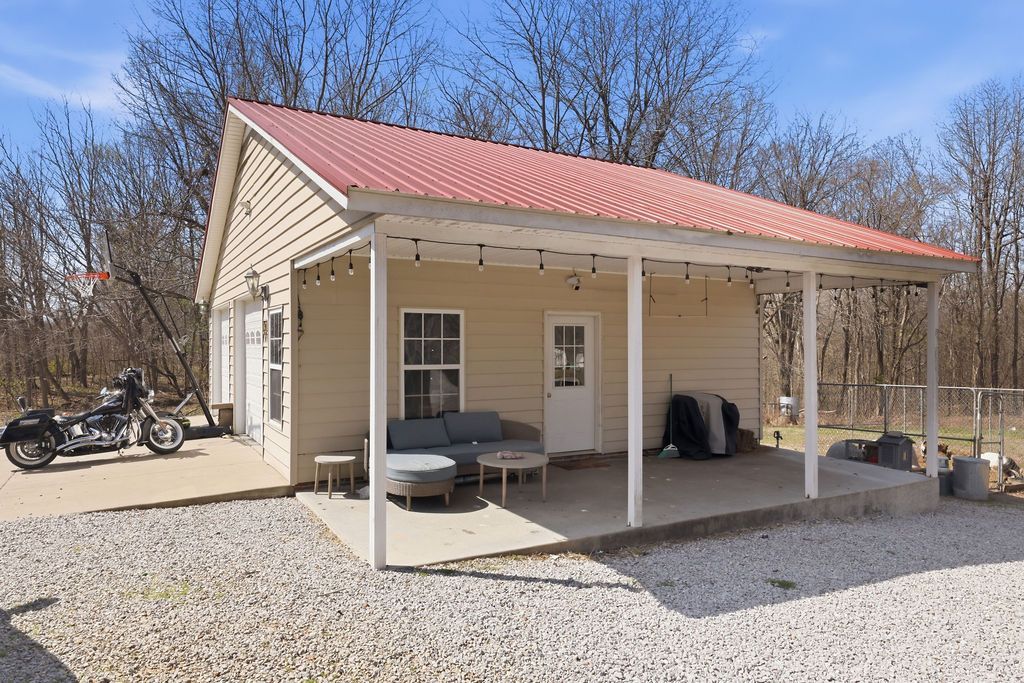 Small cream house with red metal roof, front porch, gravel yard, and motorcycles parked beside it.