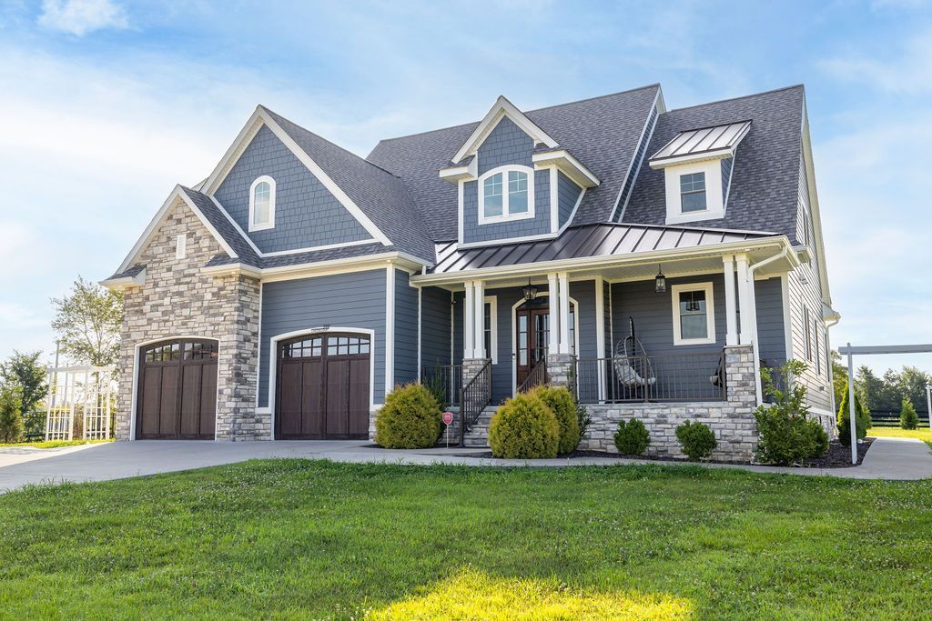 Gray two-story suburban house with dormer windows, front porch, and three garage doors on a green lawn