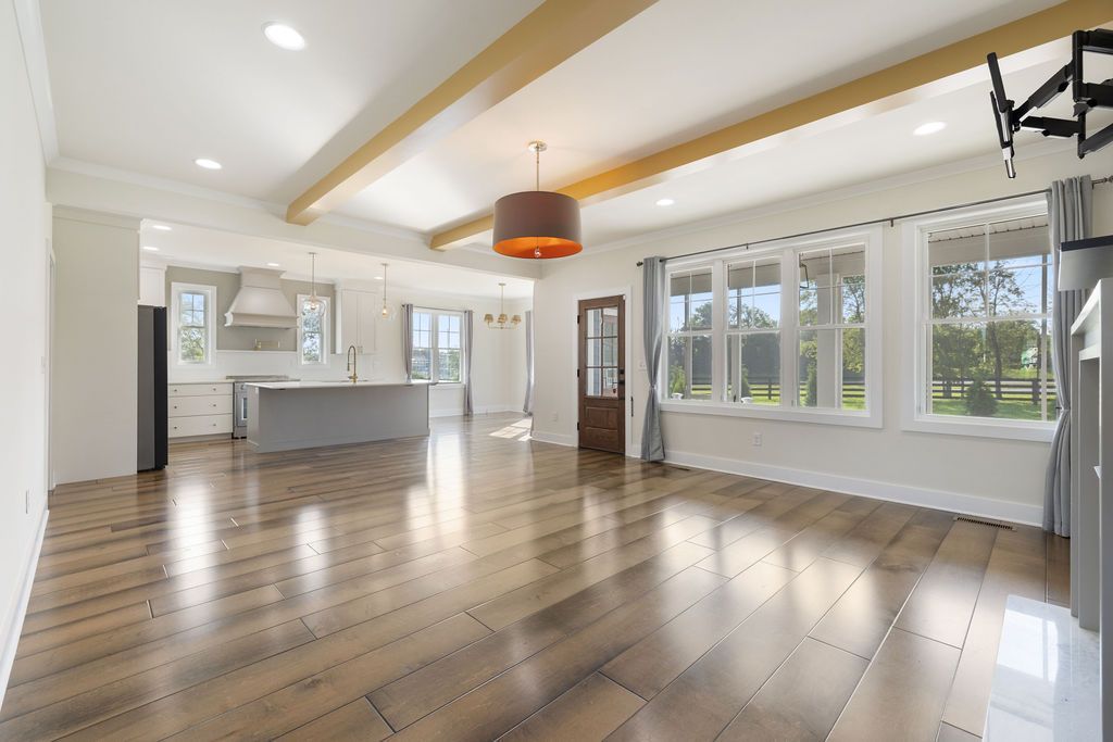Bright empty living room with hardwood floors, large windows, white walls, and a hanging pendant light