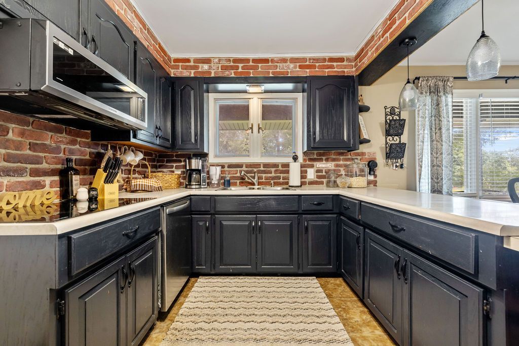Modern kitchen with dark cabinets, brick backsplash, stainless appliances, and a window over the sink.