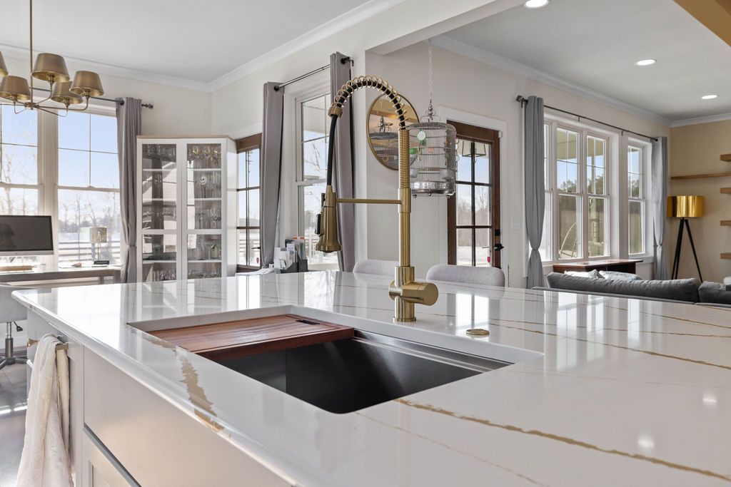 Bright modern kitchen with white island, gold faucet, and large windows overlooking water